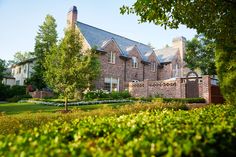 a large brick house surrounded by lush green trees and shrubbery in front of it