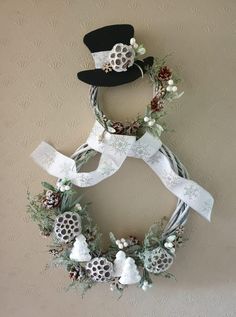 a snowman wreath hanging on the wall with pine cones and white ribbon around it