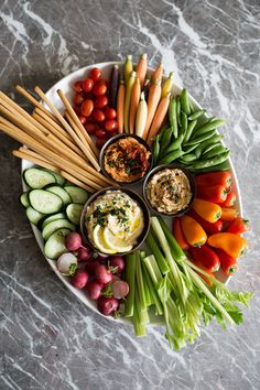 a platter filled with vegetables and dips on top of a marble countertop