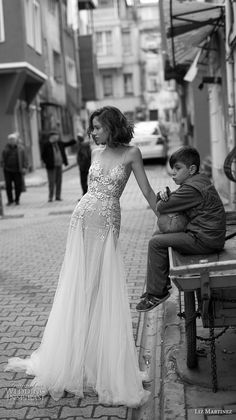 a woman in a long dress standing next to a young boy on a street bench