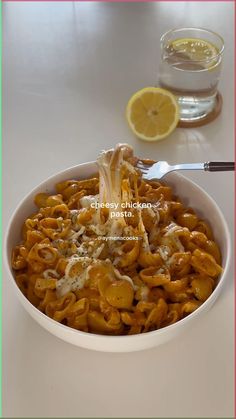 a white bowl filled with pasta and sauce next to a slice of lemon on top of a table