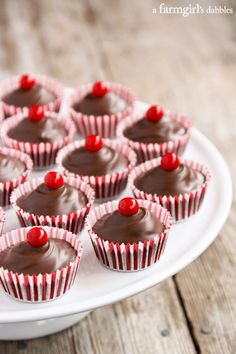 chocolate cupcakes with cherries on a white plate sitting on a wooden table