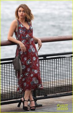 a woman in a red dress standing next to a fence and looking at the camera