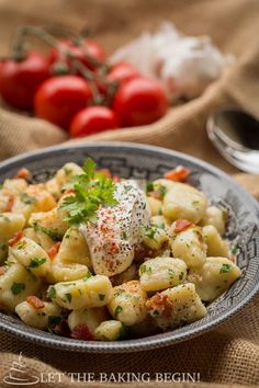 a close up of a bowl of food on a table with tomatoes in the background