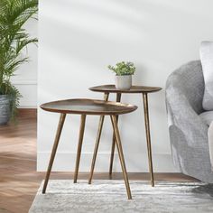 two wooden tables sitting on top of a rug in front of a gray chair and potted plant