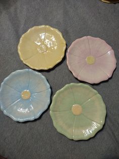 four different colored plates sitting on top of a gray cloth covered table with an object in the background