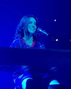 a smiling woman sitting at a piano in front of a microphone and blue light behind her