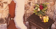 a chair and table with flowers on it next to a stone wall in the background