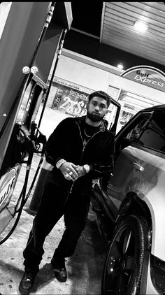 a man standing next to a car at a gas station with his hand on the fuel pump