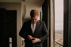 a man in a suit looking down at his watch while standing next to a window