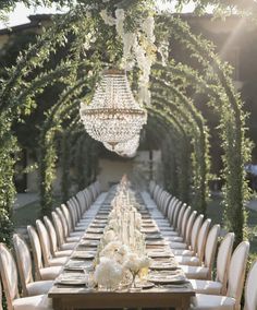 a long table with white chairs and chandelier hanging from it's ceiling