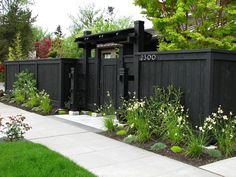 a black fence with white flowers and trees in the background