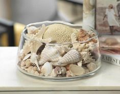 a glass bowl filled with sea shells on top of a table next to a book