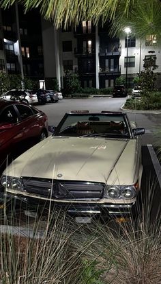 an old car is parked in front of a building at night with its lights on