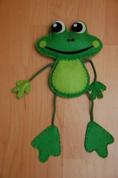 a green stuffed frog with big eyes on wooden floor next to wood paneled wall