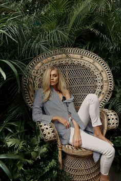 a woman sitting in a wicker chair surrounded by tropical plants and greenery, posing for the camera