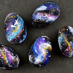 four painted rocks sitting on top of a black surface with colorful paint splattered all over them