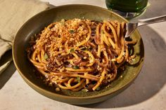 a green bowl filled with pasta and meat on top of a table next to a glass of water