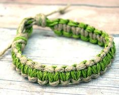 a close up of a green and white bracelet on a wooden surface with string attached to it