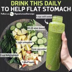 a hand holding a green smoothie next to a plate of vegetables and cucumbers