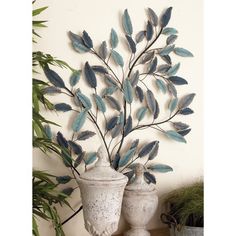 two white vases sitting next to each other on top of a wooden table with blue leaves