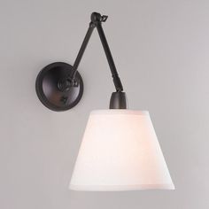 a black wall light with a white shade on the arm and an attached lamp bulb