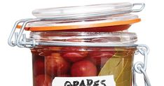 a jar filled with red apples sitting on top of a white table next to a sign that says grapes