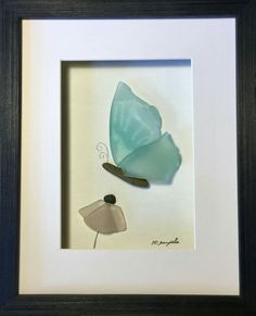 a blue and white glass butterfly in a black frame on the wall next to a flower