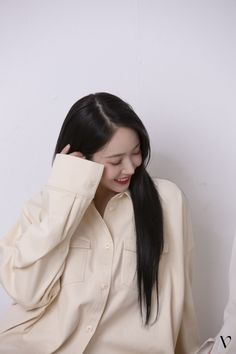 a woman with long black hair wearing a white shirt and holding her hand to her head