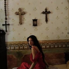 a woman in a red dress is sitting on a bed with crosses above her head