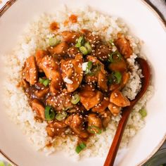 a white plate topped with chicken and rice next to a wooden spoon on top of a table