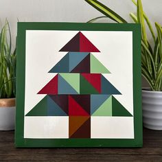 a green frame with a colorful christmas tree on it and potted plants in the background