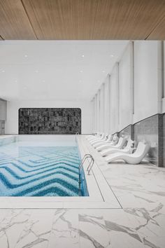 an indoor swimming pool surrounded by white marble flooring and walls with large windows on each side