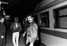 black and white photograph of people standing next to a train at night with one man wearing a leather jacket