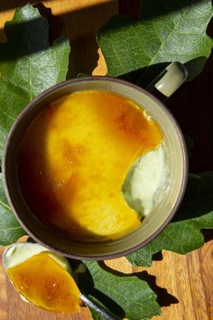 a cup filled with liquid sitting on top of a wooden table next to green leaves