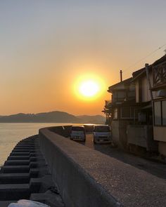 the sun is setting over the water and cars are parked on the side of the road