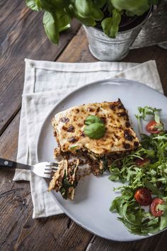 a white plate topped with pizza next to a salad and a fork on top of a wooden table