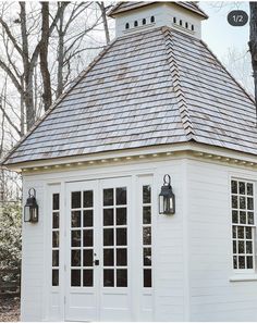 a white gazebo with two lanterns on the roof and a brown shingled roof