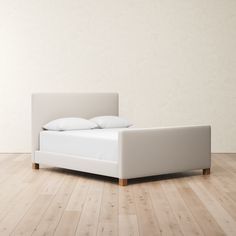 a bed sitting on top of a wooden floor next to a white wall with pillows