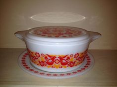 a white casserole with red and yellow designs on it