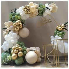 balloons and greenery are arranged on the floor in front of a backdrop with gold, white and green decorations