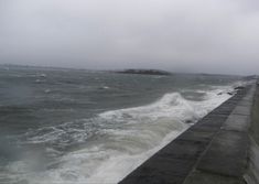 the ocean is choppy and stormy with waves crashing against the concrete wall on either side