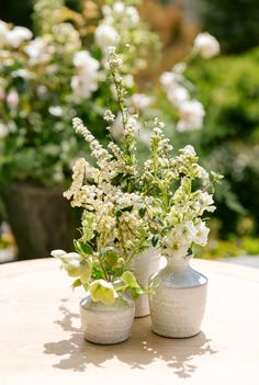 two white vases with flowers in them sitting on a table next to each other