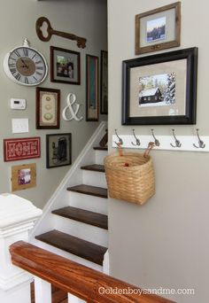 there is a basket hanging on the wall next to some stairs with pictures above it