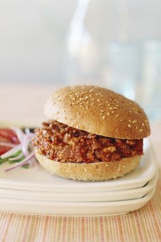 a sloppy joe sandwich on a plate with tomatoes and lettuce next to it