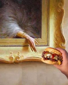 a hand holding a sandwich in front of a painting