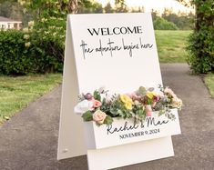 a welcome sign with flowers and greenery on it