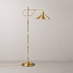 a floor lamp that is on top of a table next to a white wall with a gold colored shade