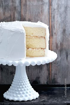 a white cake sitting on top of a white plate next to a wooden wall with polka dots