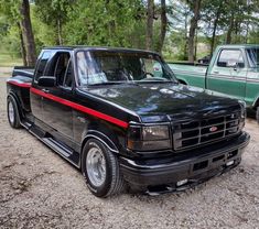 two pickup trucks parked next to each other in the dirt near some trees and bushes